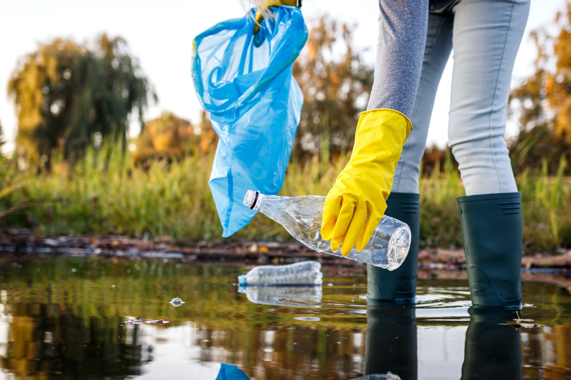 Volunteer picking up plastic bottle from polluted lake